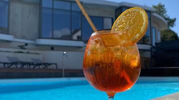 A glass with a beverage and a lemon slice, placed by a pool with a building in the background.