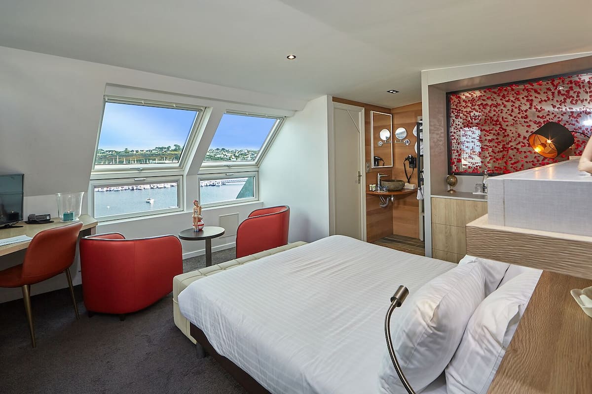 Ett hotellrum med en säng, ett skrivbord med en dator, en stol och ett fönster med utsikt över vattnet.