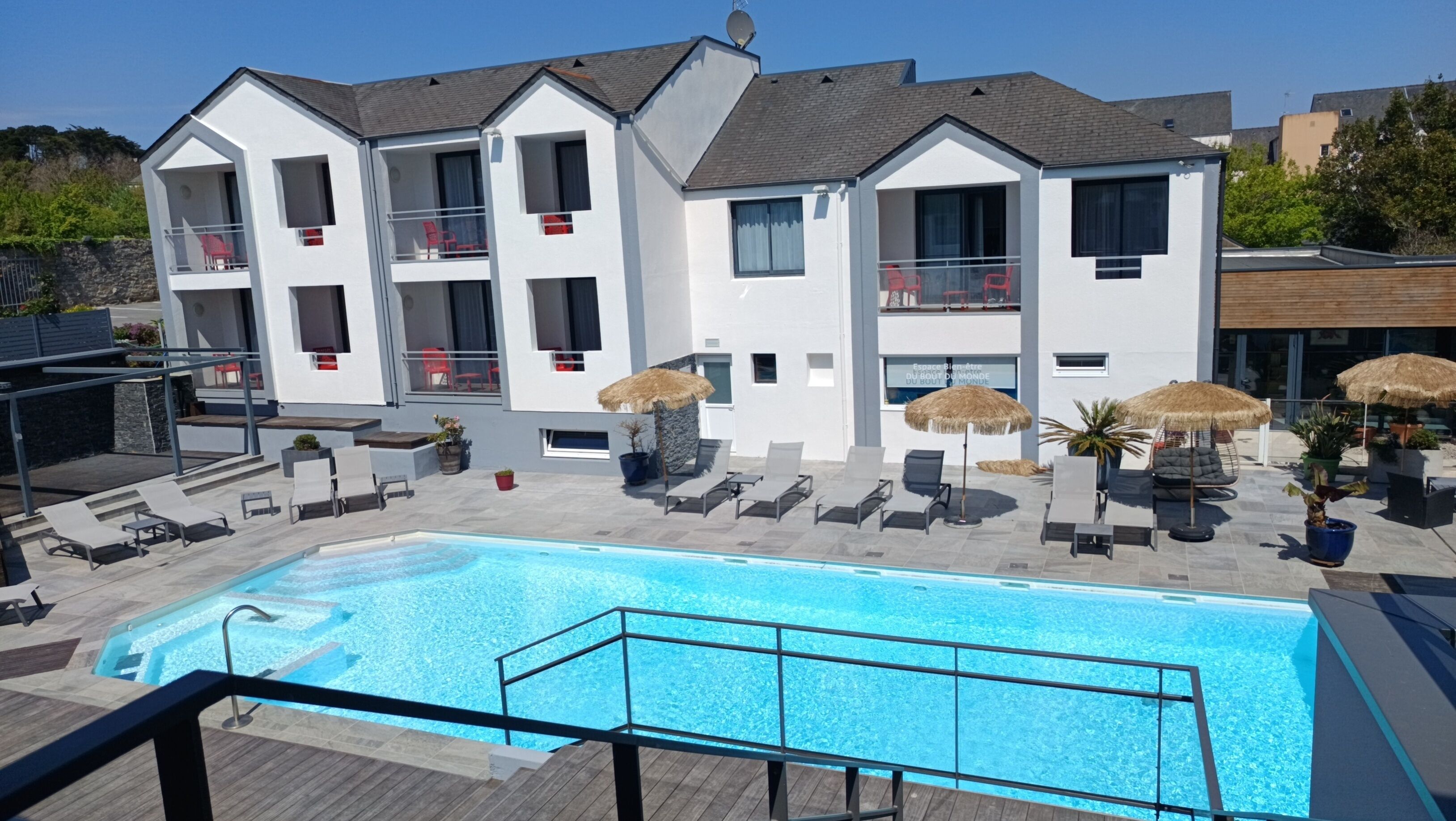 Un hotel moderno con piscina, tumbonas y sombrillas de paja.