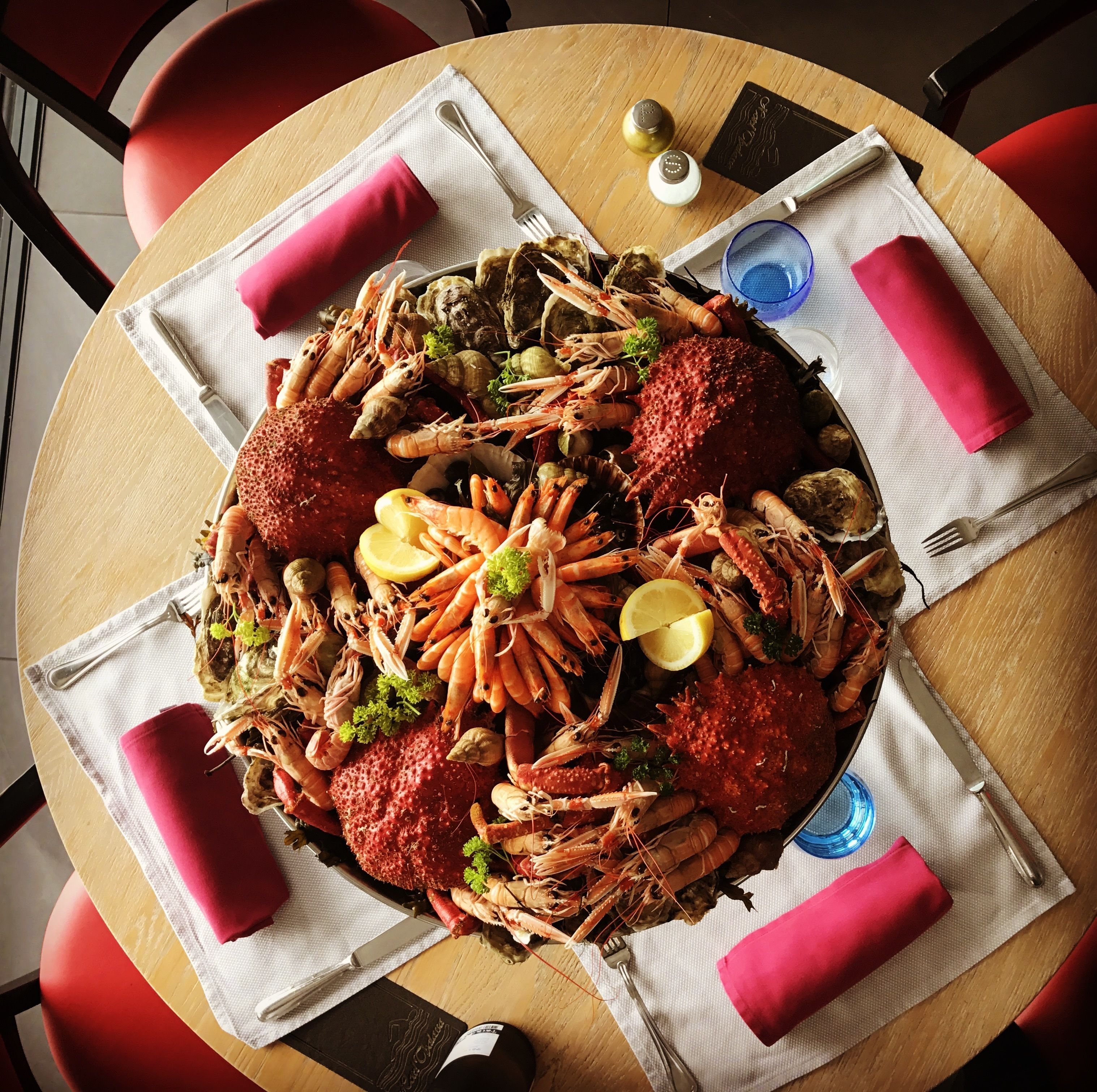 A seafood platter on a round table with a white napkin, a fork, a knife, and a glass of water.