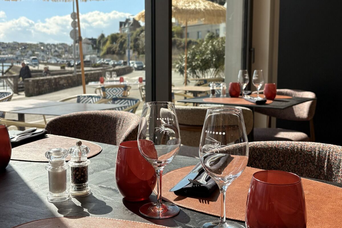 Un restaurant doté d’une terrasse, offrant une vue sur le port, et dont les tables sont dressées avec des verres à vin et des salières et poivrières.