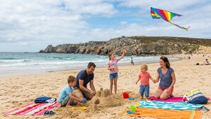 A beach scene with people, a colorful kite, and a sandy area with a beach umbrella.