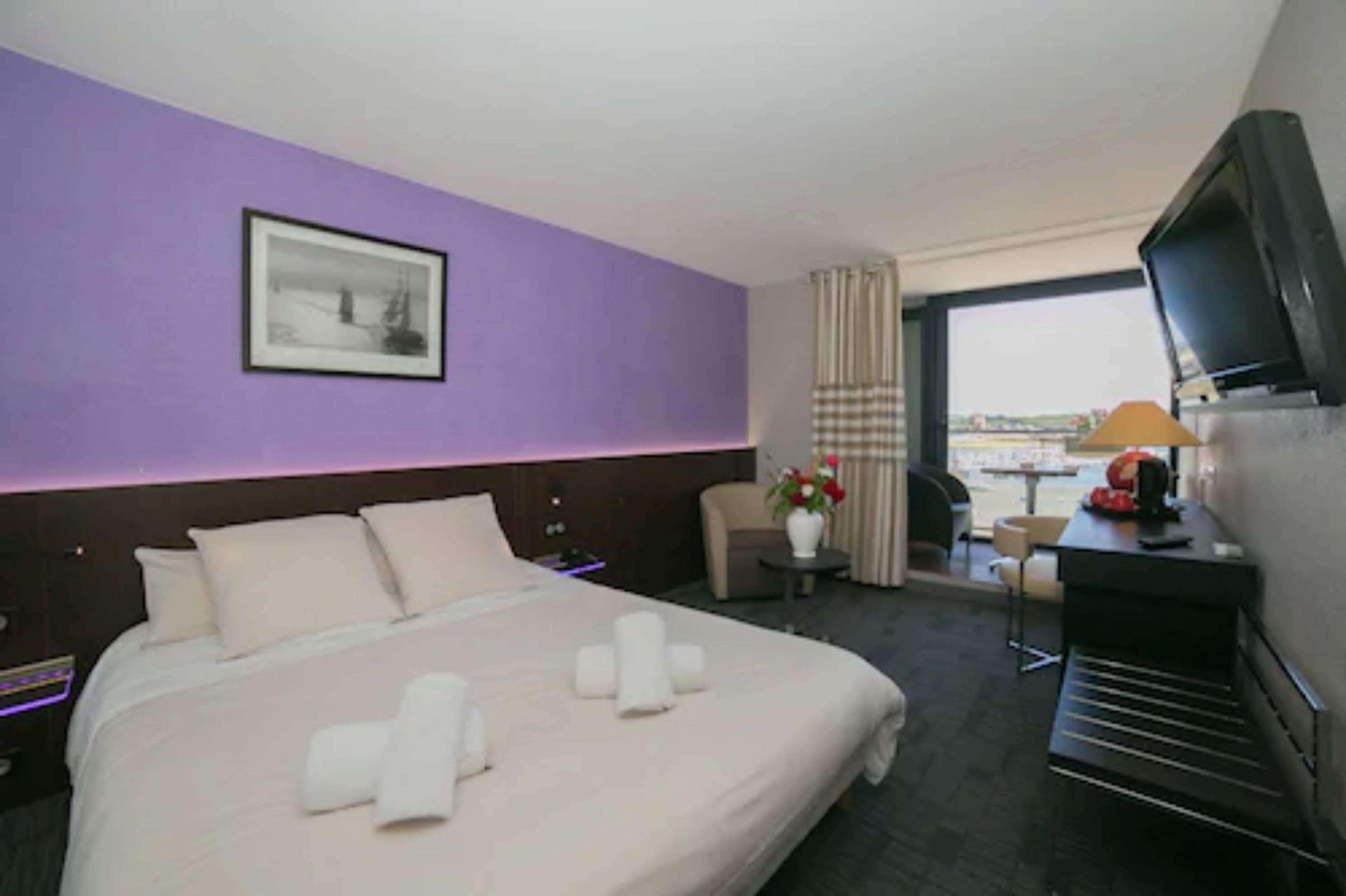 Ein Hotelzimmer mit einem großen Bett, einem Schreibtisch mit Computer, einem Fernseher und einem Fenster mit Blick.