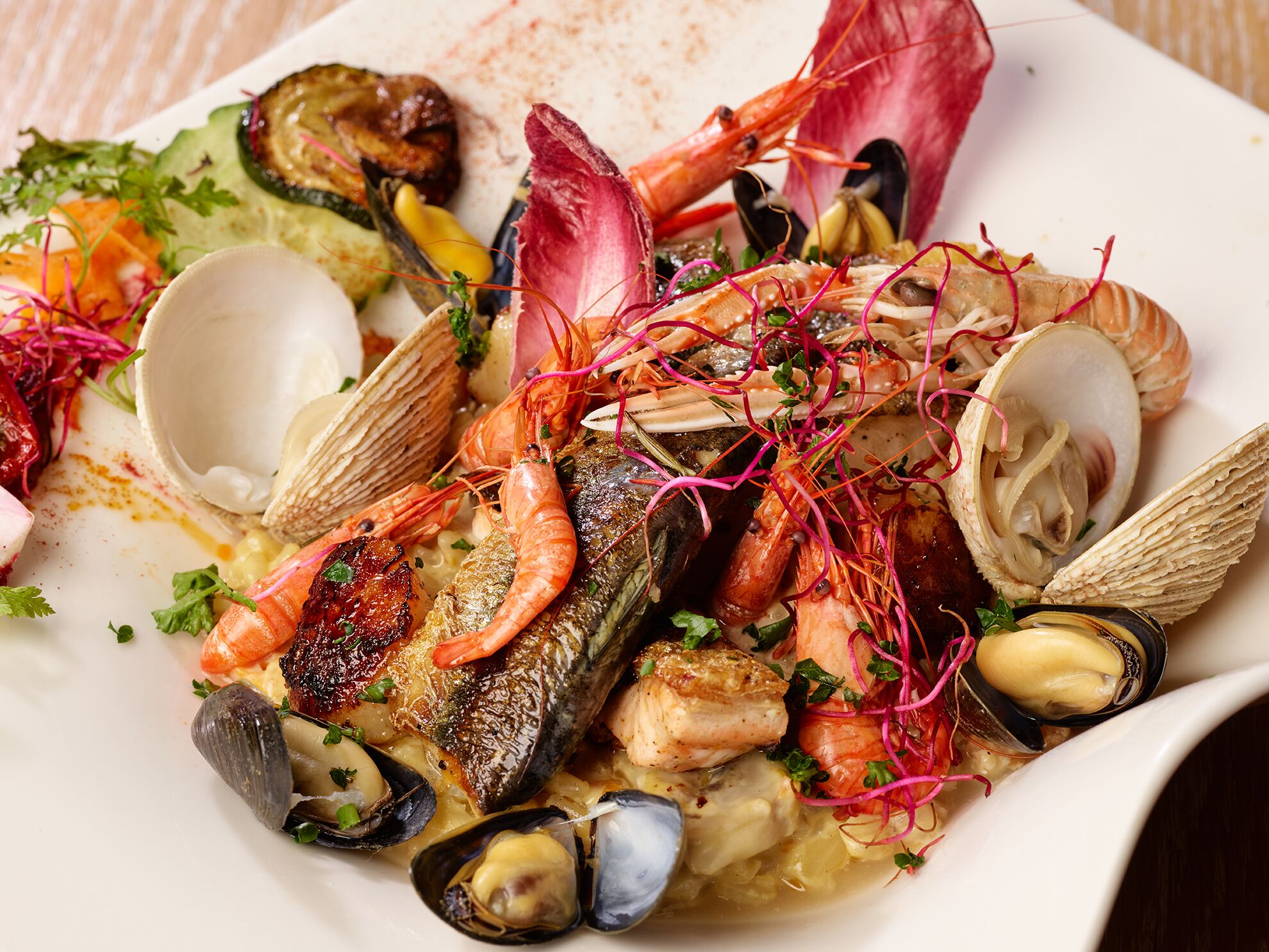 A seafood dish with mussels, clams, shrimp, and fish, garnished with herbs and microgreens.