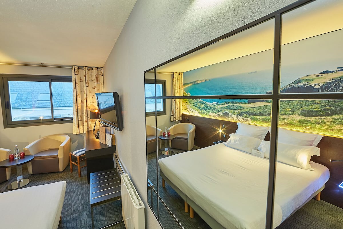 Ett hotellrum med en säng, två fåtöljer, ett skrivbord med en tv och ett stort fönster med utsikt över kusten.