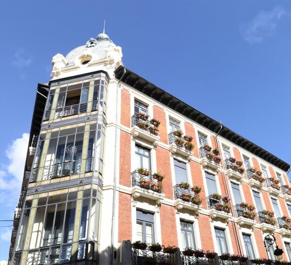 A multi-story building with a corner entrance, large windows, and balconies with flower boxes.