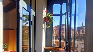 En smal balkon med et træbord og stole, store vinduer og blomsterkasser hængende ned.
