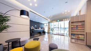 A modern lobby with seating areas, a reception desk, and a display of amenities.