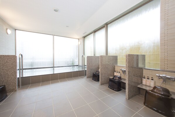 Ein modernes Badezimmer mit großen Fenstern, gefliestem Boden und mehreren Waschbecken mit Seifenspendern.
