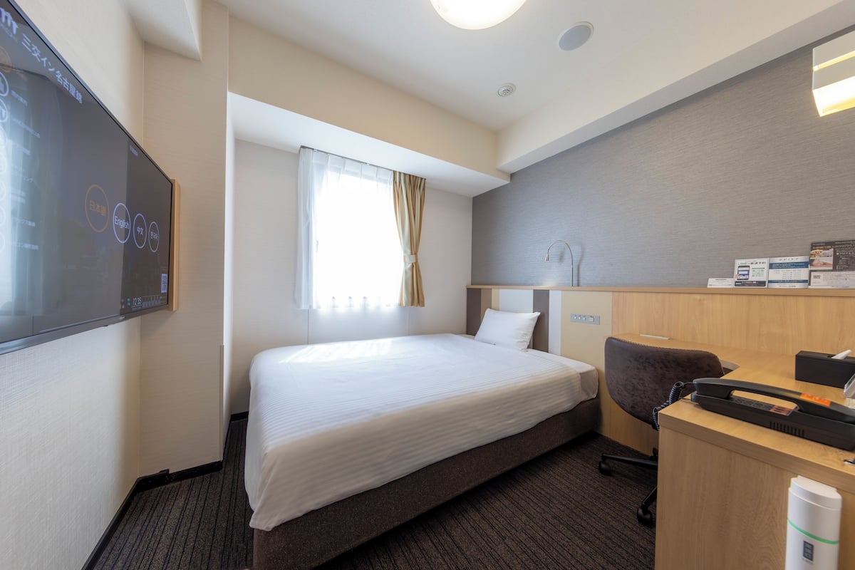 Habitación de hotel con cama, escritorio, silla y una pantalla de televisión mostrando un menú.