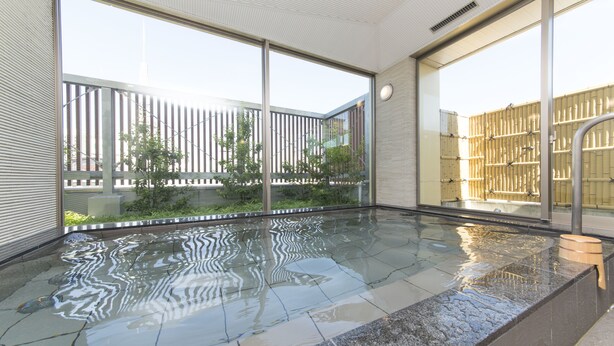 A modern indoor swimming pool with clear glass walls, a tiled floor, and a view of a cityscape.