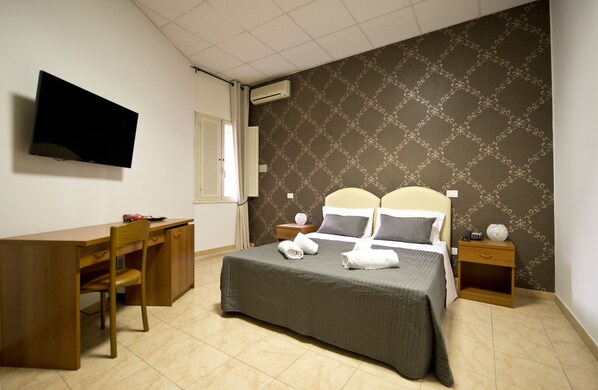 A hotel room with a bed, a desk, a chair, a television, and a nightstand.