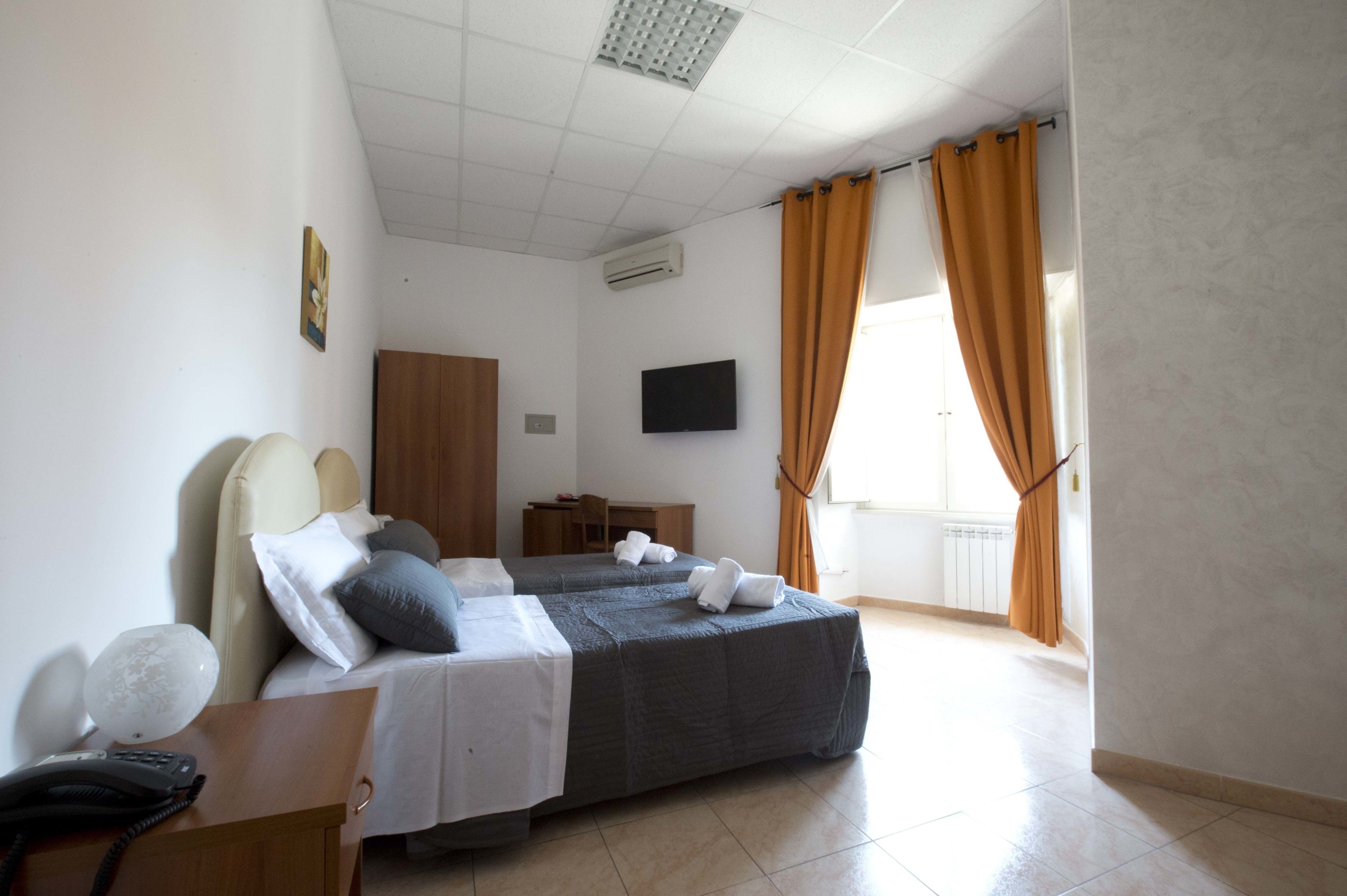 A hotel room with two beds, a desk with a telephone, a television on the wall, and a window with curtains.