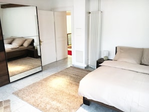 A bedroom with a bed, a large mirror, a radiator, and a door leading to another room.