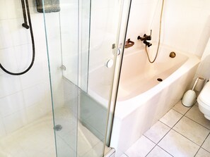 Un baño moderno con ducha de vidrio, una bañera blanca y un inodoro.