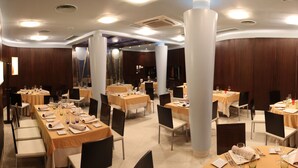 Een restaurant met meerdere ronde tafels, elk voorzien van witte tafelkleden, stoelen en netjes gedekte tafels met borden, glazen en bestek.