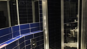 Een badkamer met een glazen douchecabine, een wit wastafelmeubel en blauwe betegelde wanden.