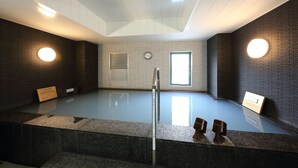 A modern indoor swimming pool with a skylight ceiling, a clock, and wooden benches. - Sanco Inn Toyota (Toyota)