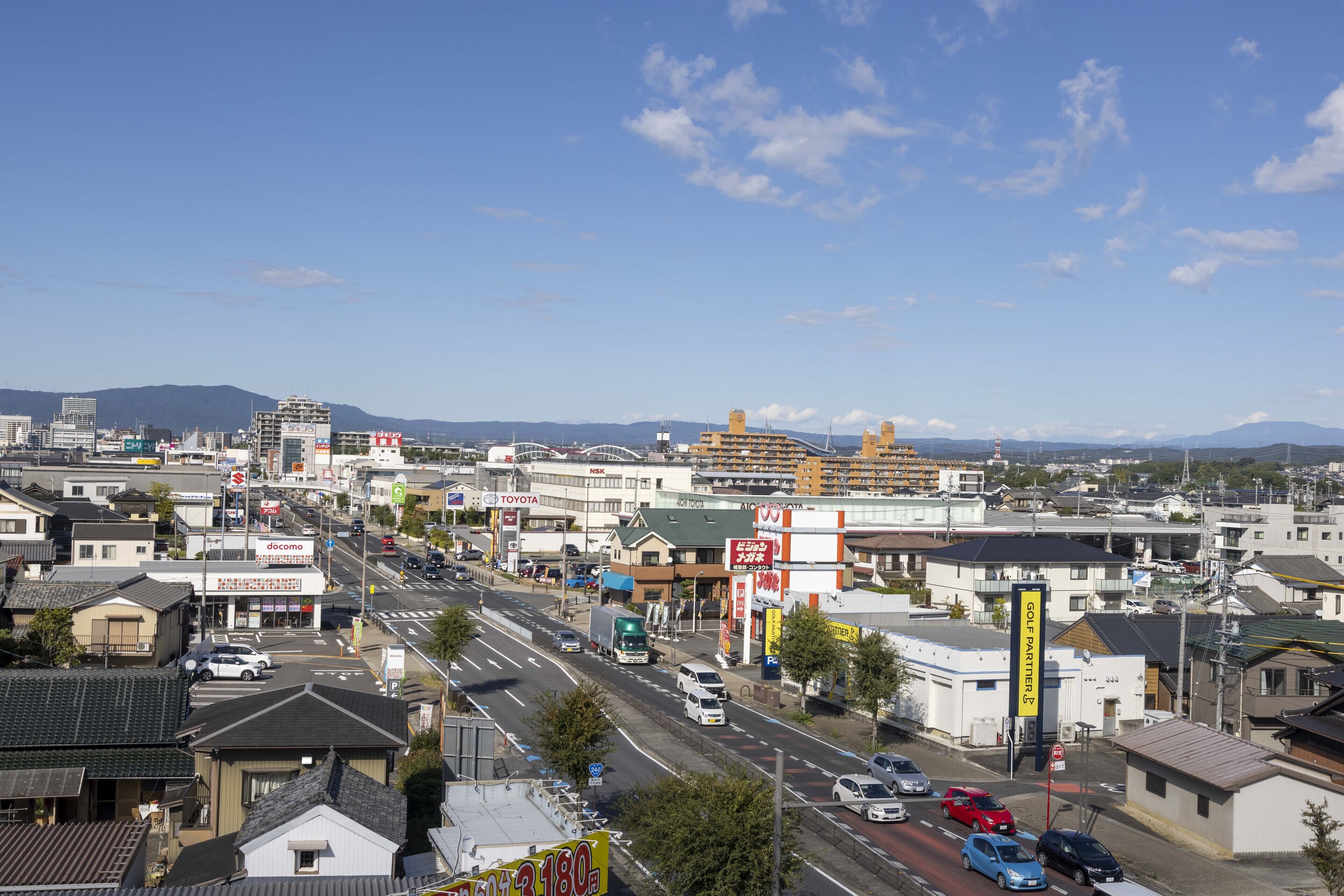 A cityscape with a wide road, various buildings, and a clear sky.