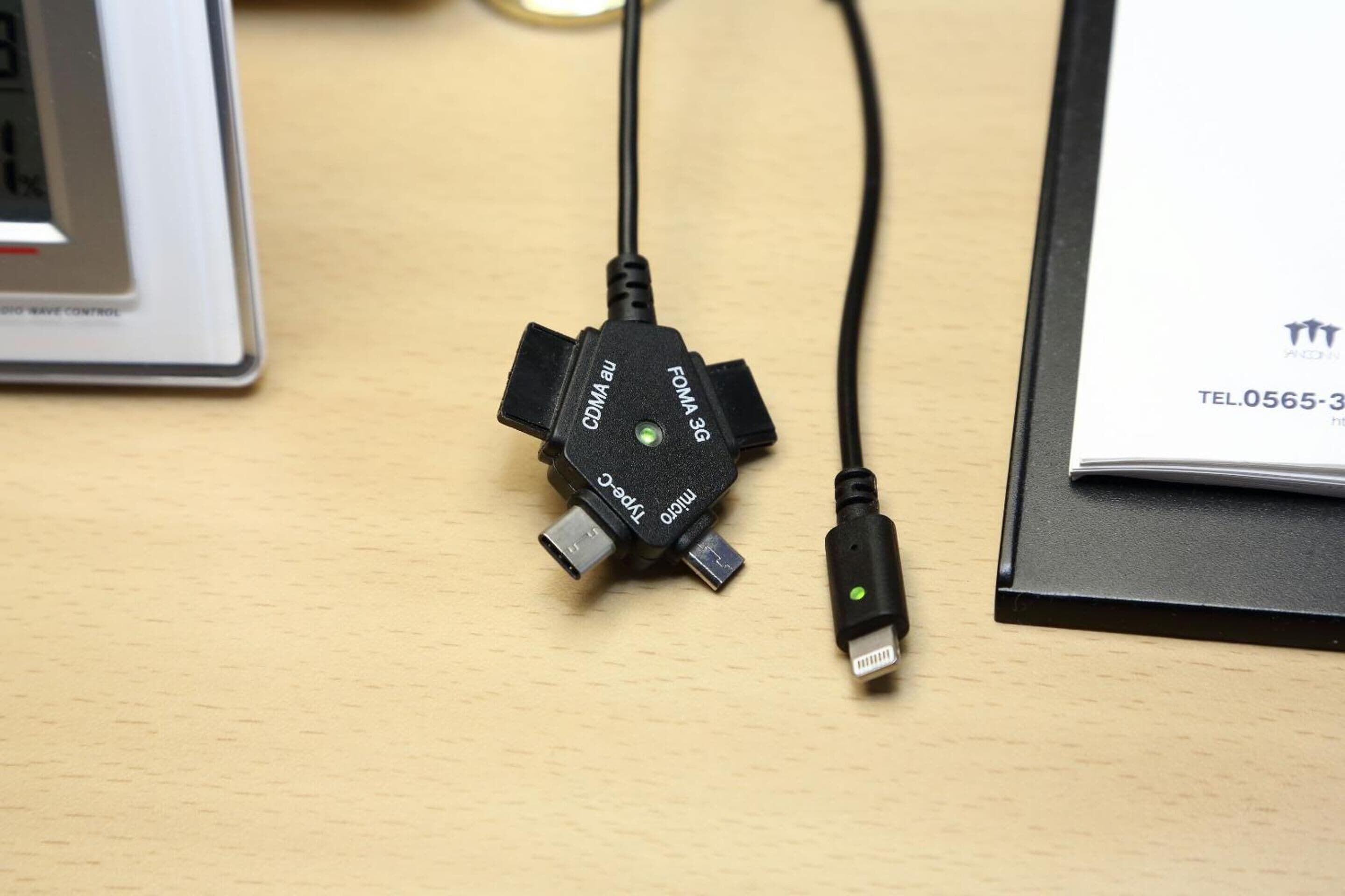 A USB-C to Type-C adapter with a green power button on a wooden surface.