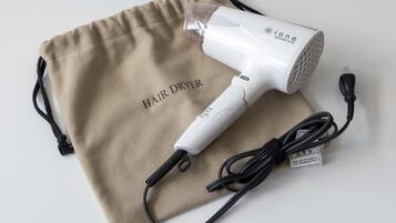 Un secador de pelo con un cable de carga y una bolsa de tela color beige con la etiqueta 'HAIR DRYER'.