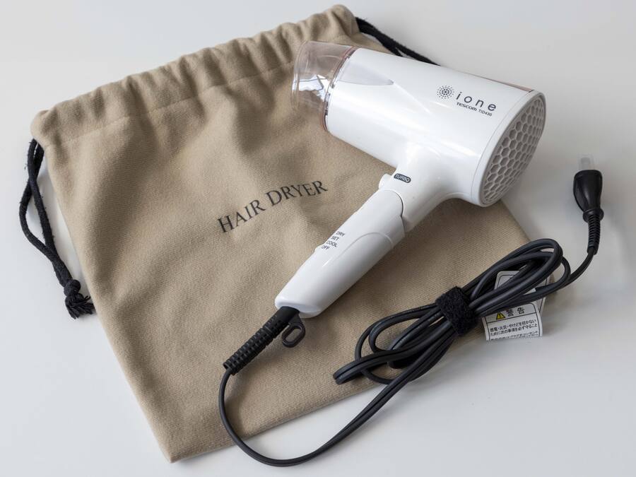 Un secador de pelo con un cable de carga y una bolsa de tela color beige con la etiqueta 'HAIR DRYER'.