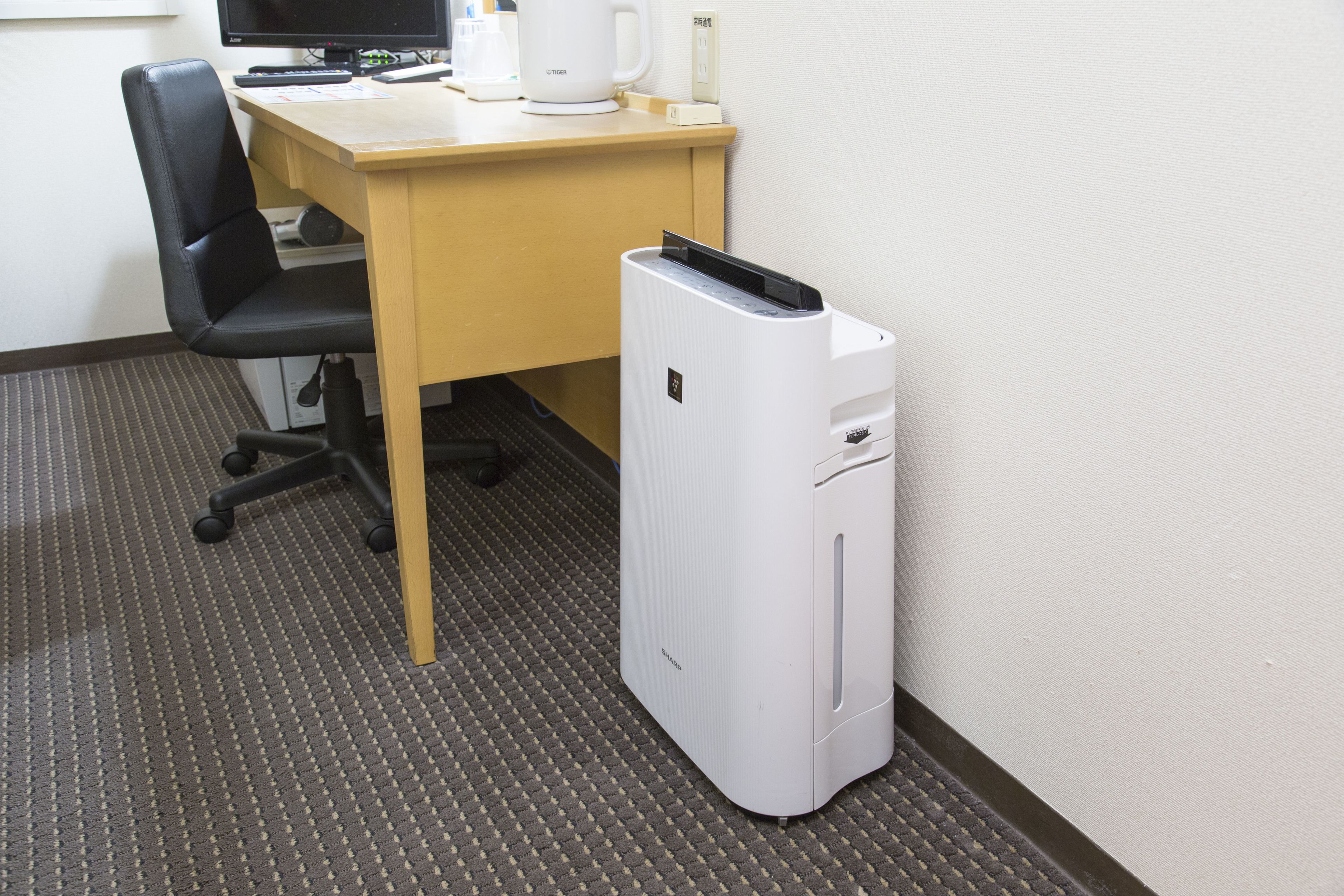 A hotel room with a desk, a black office chair, a white printer, and a coffee maker.