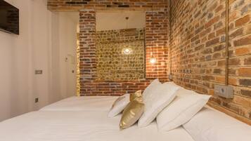 A hotel room with a brick wall, a bed with white linens, and a stone wall in the background.