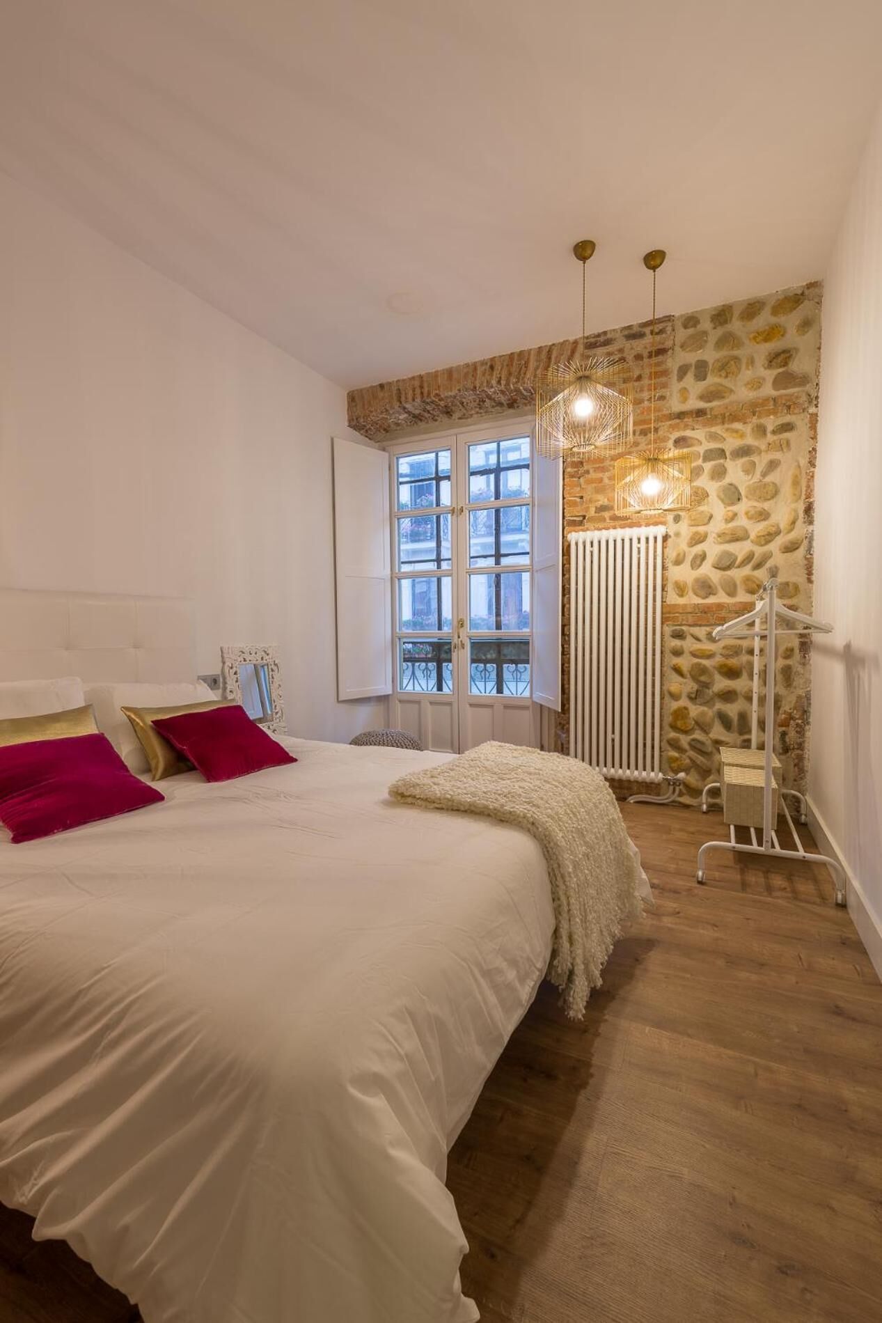 Un dormitorio con una cama grande, una pared de piedra, un radiador y una ventana con vistas.