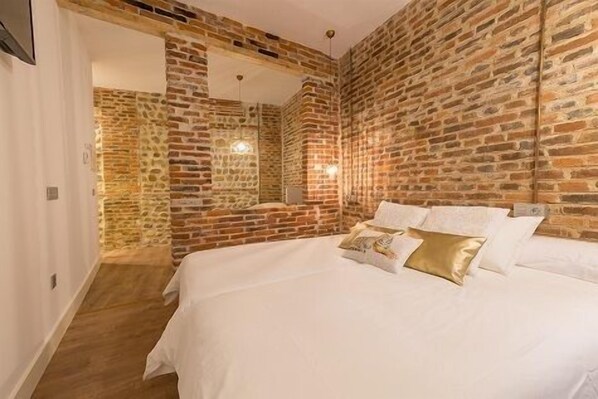 A bedroom with a brick wall, a bed with white bedding, and a mirror. - Hostal Albany Ancha (León)