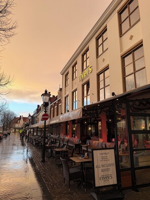 Calle con mesas al aire libre, un restaurante llamado 'Rivers' y un letrero que anuncia 'buffet todo incluido'.