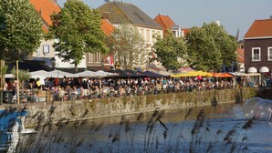 Een markt aan de rivier in de open lucht, met mensen en tenten, omringd door gebouwen en bomen.