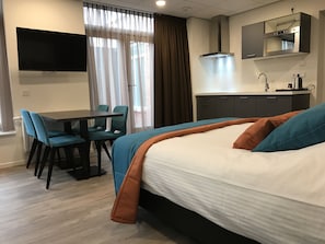 A hotel room with a bed, a desk, two chairs, a TV, a mirror, and a kitchenette.