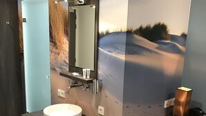 Een moderne badkamer met een grote spiegel, een rond wastafel, een meubel met opbergruimte, een wandlamp en een blauwe stoel.