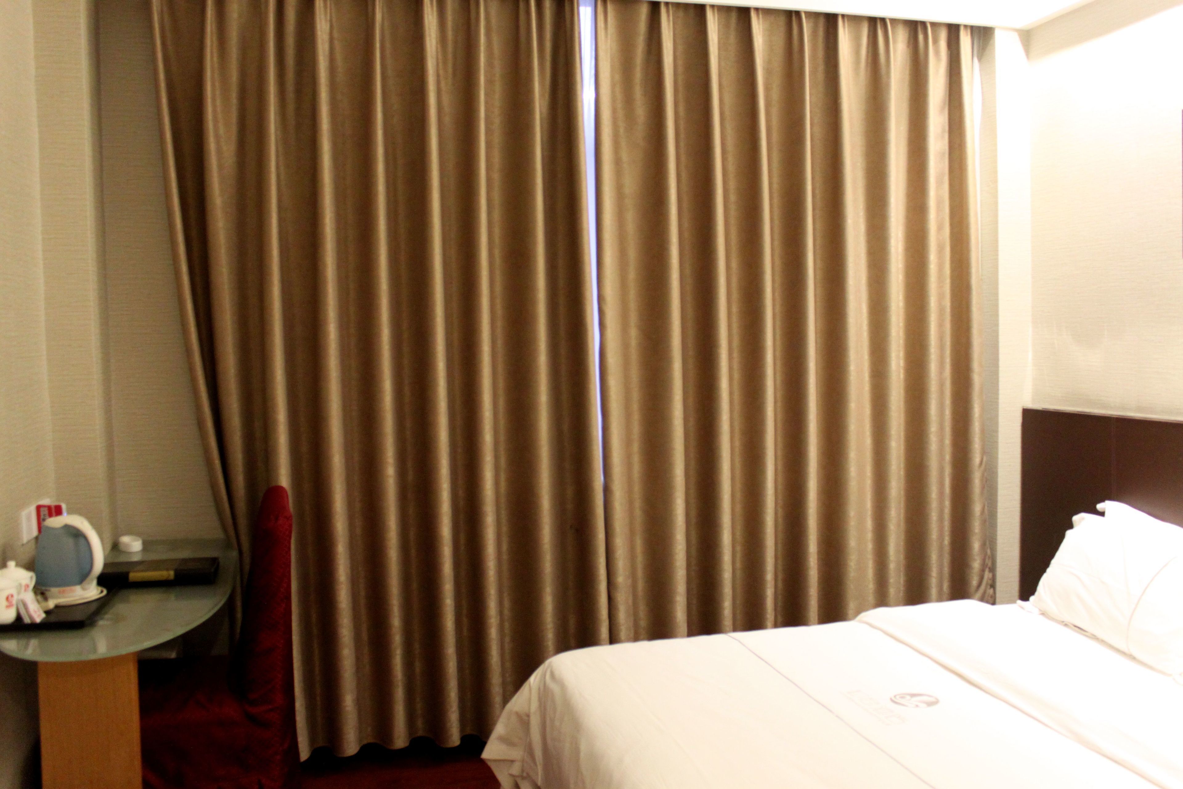 A hotel room with a bed, a desk with a lamp, and a window with curtains.