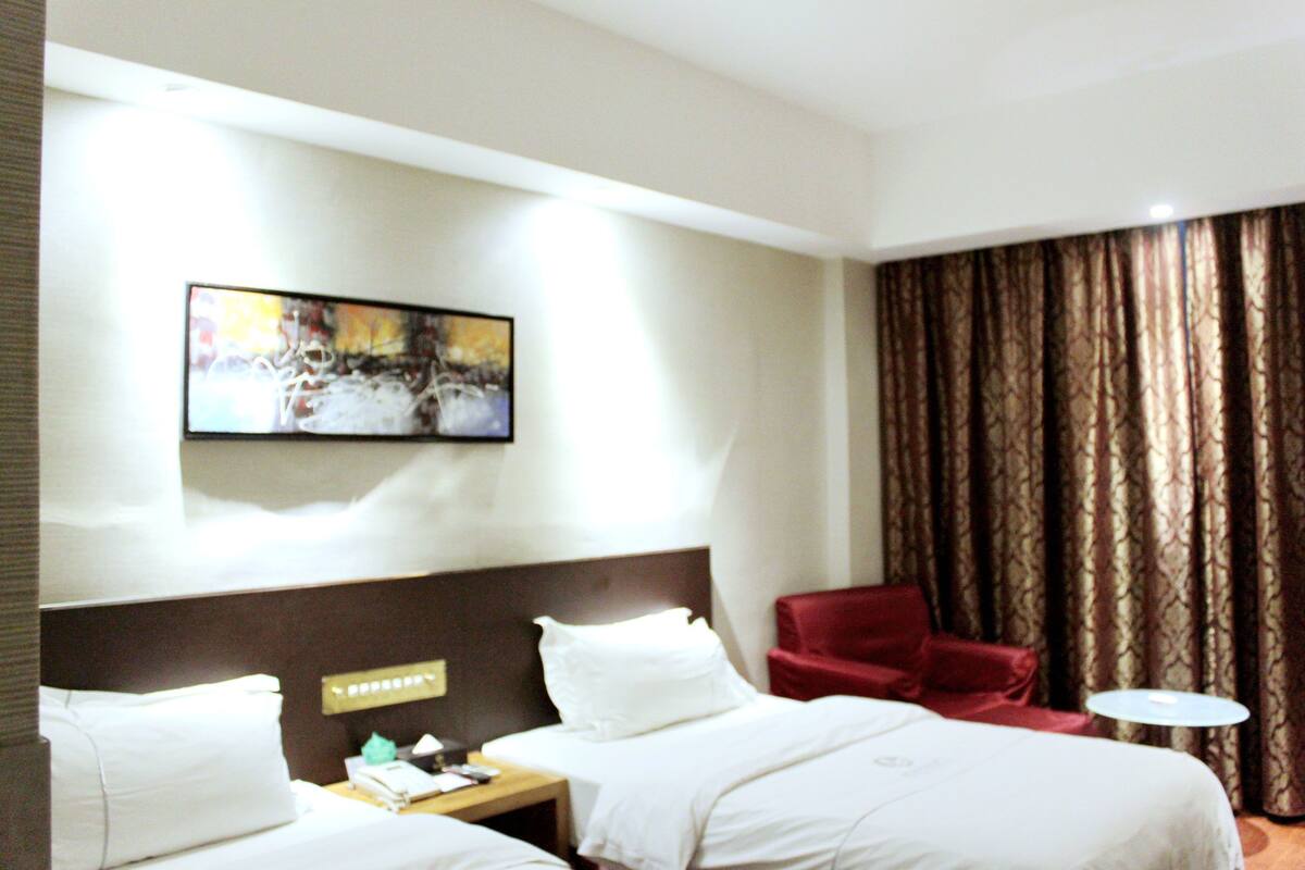 A hotel room with a bed, a red armchair, a small round table, and a painting on the wall.