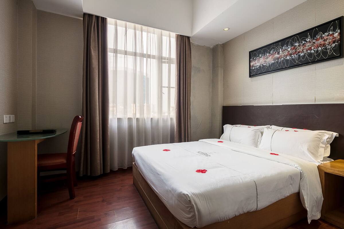 A hotel room with a bed, a desk, a chair, and a large window with curtains.