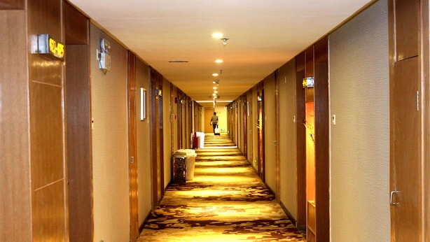 A hotel hallway with carpeted floors, wooden doors, and a person walking down the corridor. - Huangpu Hotel (Guangzhou)