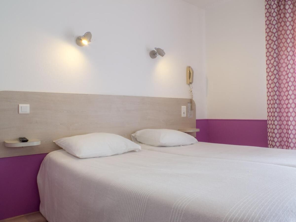 A hotel room with a bed, two bedside tables, a wall-mounted telephone, and a light fixture.