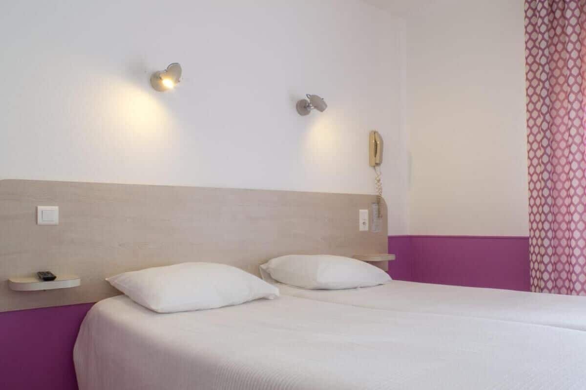 Ein Hotelzimmer mit einem Bett, zwei Nachttischen, einem fest montierten Telefon und einer Lampe.