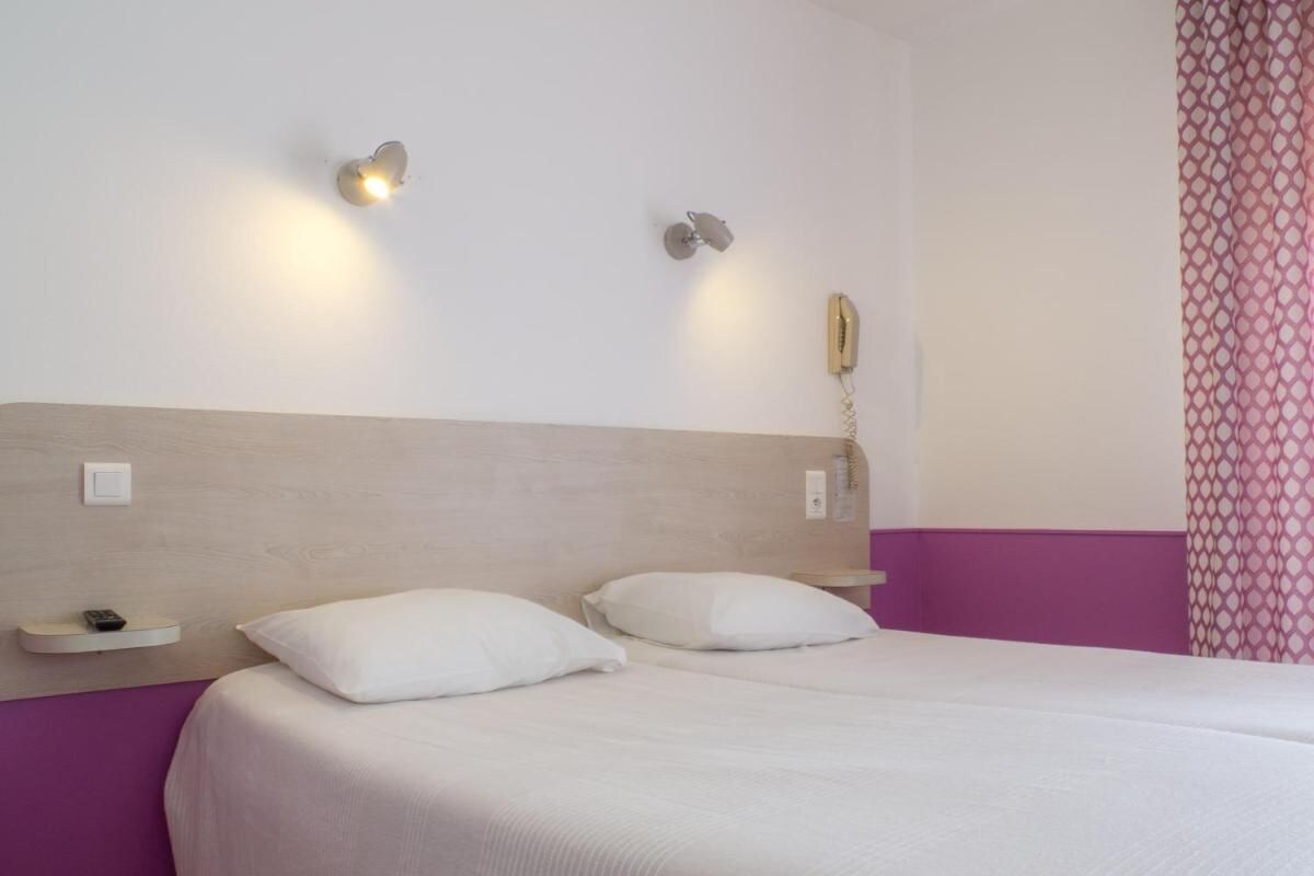 Una habitación de hotel con una cama, dos mesitas de noche, un teléfono en la pared y una lámpara.