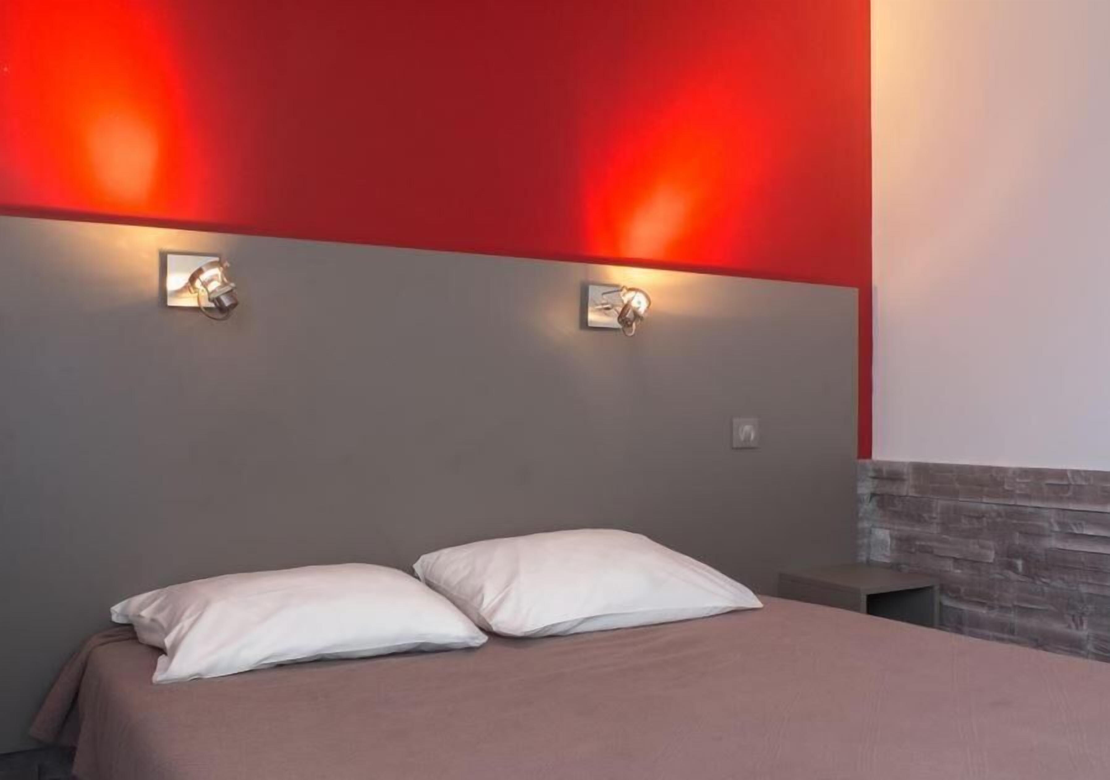 A bed with two pillows, a red wall, and two wall-mounted light fixtures.