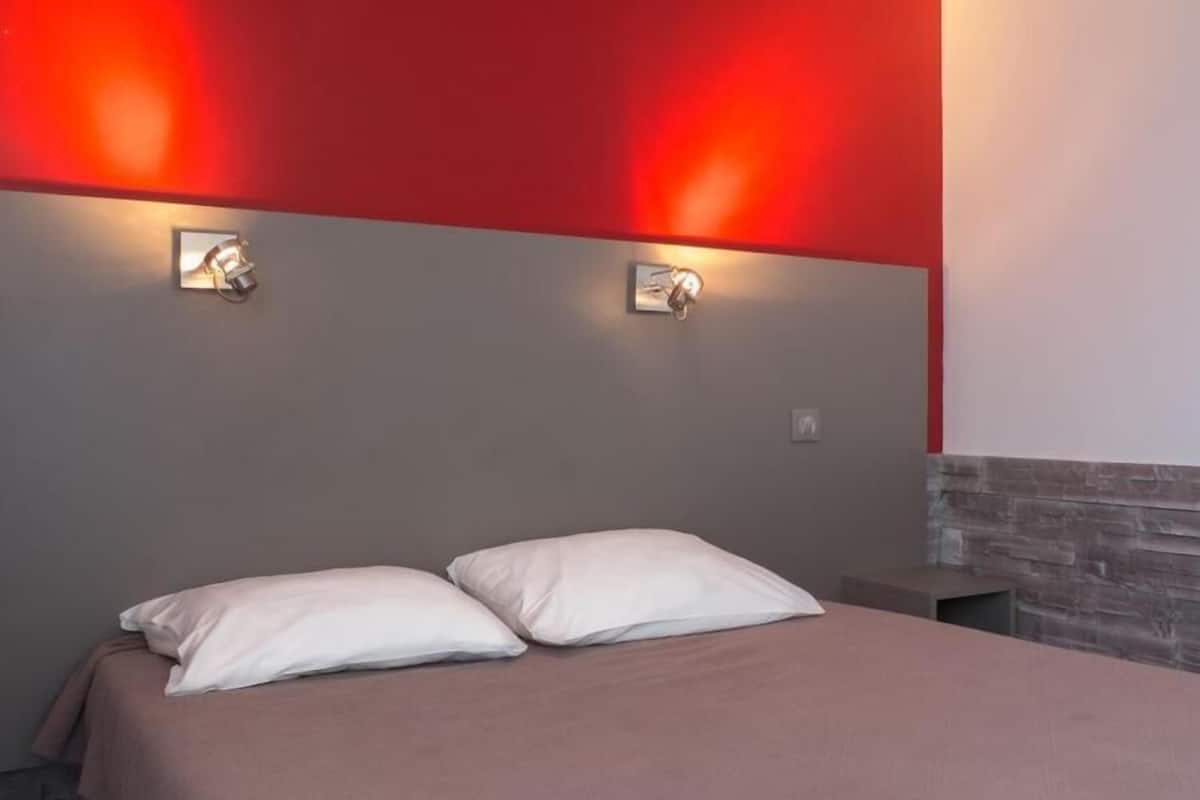 Ein Bett mit zwei Kissen, einer roten Wand und zwei Wandleuchten.