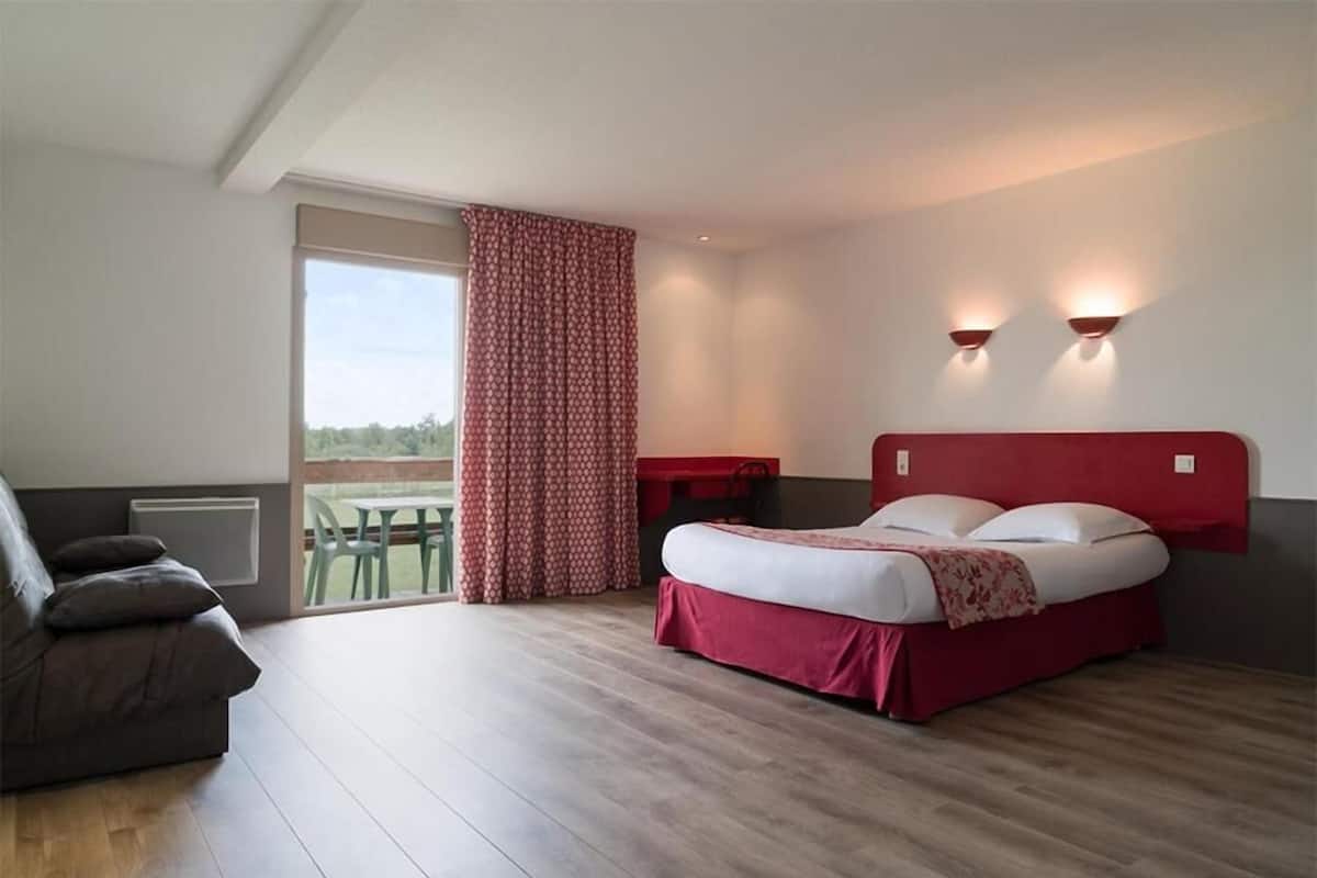Ein Schlafzimmer mit Bett, Sofa, einem Fenster mit Vorhängen und Blick auf Grünflächen.