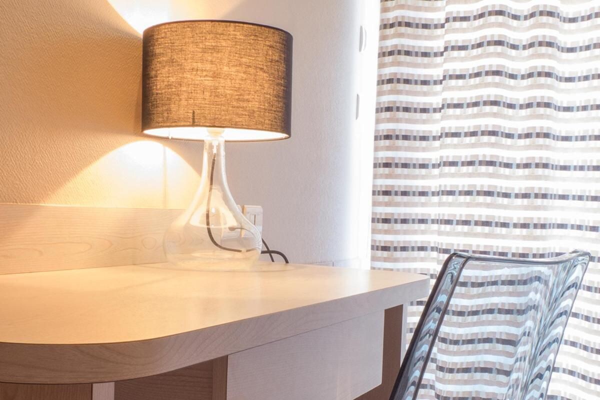 Un baño moderno con encimera curva, una lámpara de pared y cortina de ducha a rayas.
