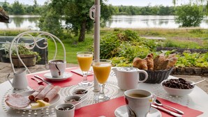 Une table de petit-déjeuner avec des croissants, du pain, du chocolat et du café, le tout disposé devant un paysage offrant une vue sur le lac.