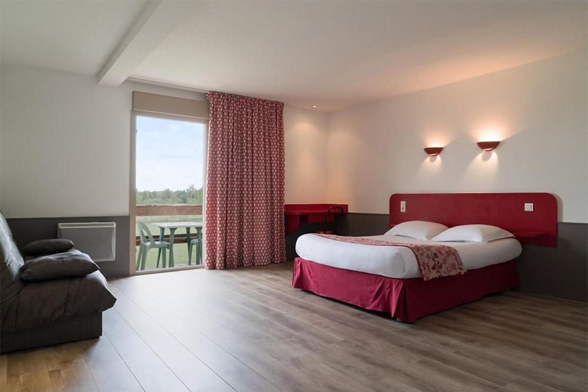 Un dormitorio con cama, sofá, ventana con cortinas y vista a zonas verdes.