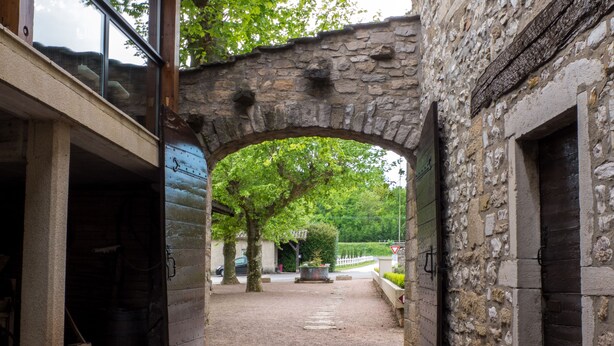 Un arc en pierre mène à une cour où se trouvent un vélo, un banc en bois et une plante en pot.