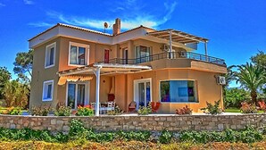 Una casa de dos pisos con balcón, ventanas grandes y un muro de piedra al frente.