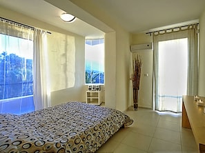 Ein Schlafzimmer mit Bett, Fenster, einem kleinen Tisch und einem Balkon.